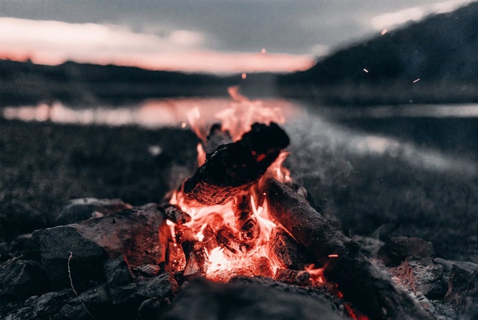 Bright Bonfire Near Lake And Mountains At Night